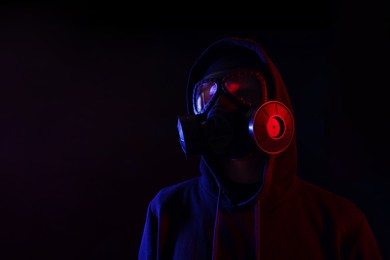 Man wearing gas mask in color lights on black background. Space for text