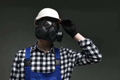 Worker in gas mask and helmet on grey background, low angle view