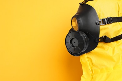 Worker in gas mask on yellow background, closeup. Space for text