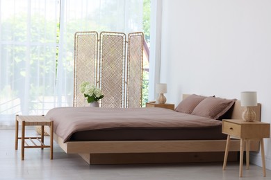 Photo of Folding screen, comfortable bed, ottoman and bedside tables in room