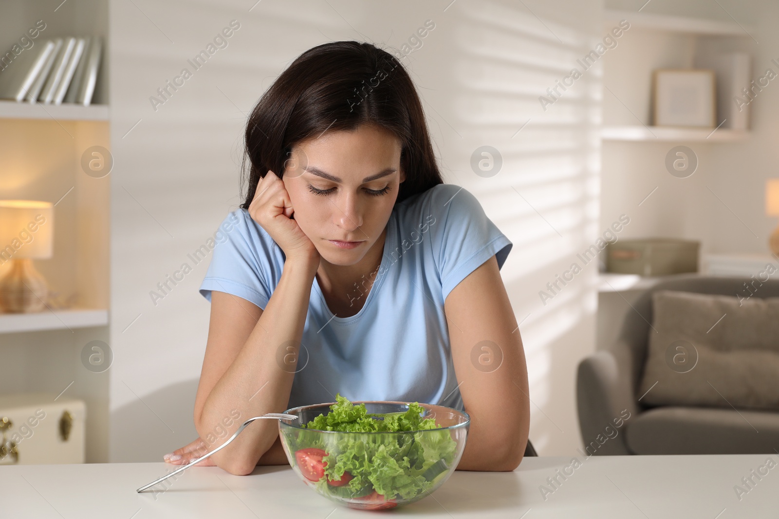 Photo of Eating disorder. Sad woman near bowl with salad at white table indoors