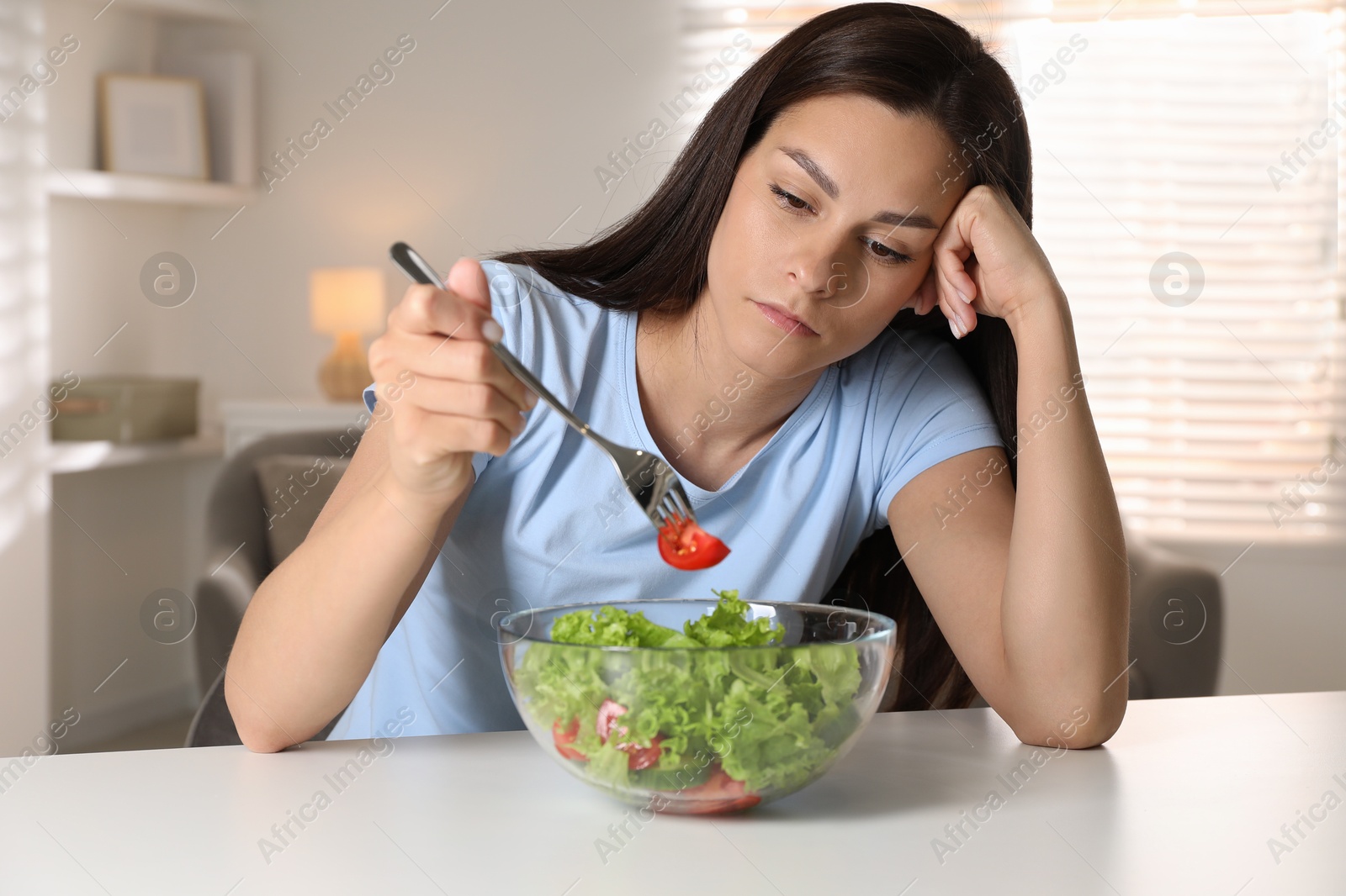 Photo of Eating disorder. Sad woman holding fork with tomato over bowl at table indoors