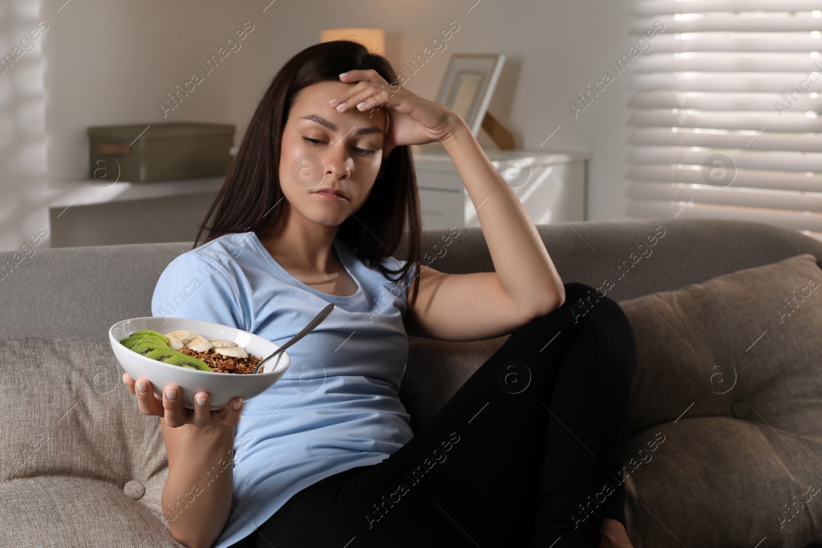 Photo of Eating disorder. Sad woman with healthy meal on sofa indoors