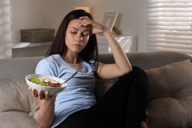 Eating disorder. Sad woman with healthy meal on sofa indoors