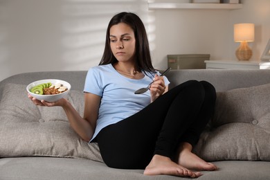 Photo of Eating disorder. Sad woman with spoon and healthy meal on sofa indoors