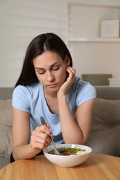 Eating disorder. Sad woman holding spoon near bowl with granola, kiwi and banana at wooden table indoors