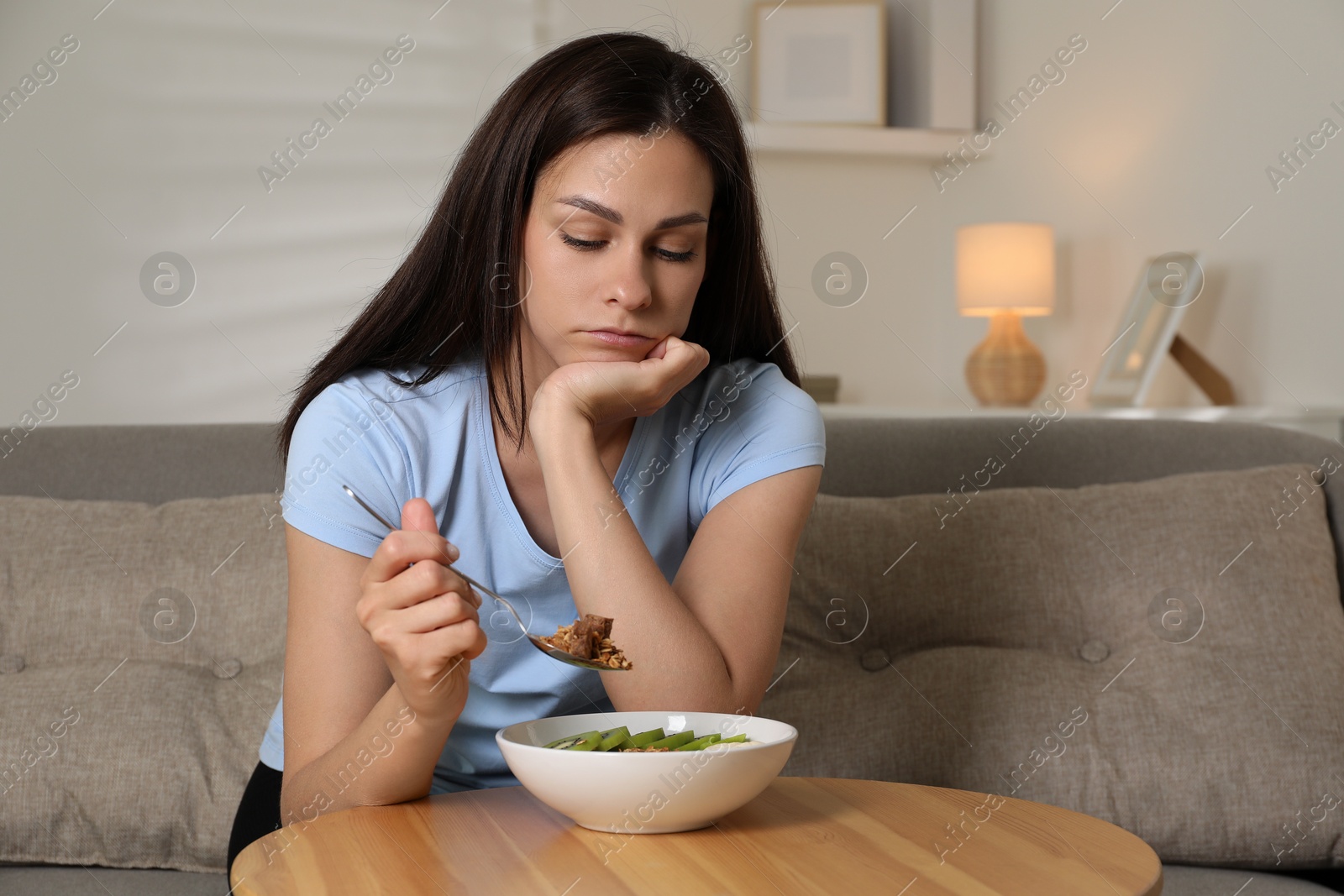 Photo of Eating disorder. Sad woman holding spoon with granola over bowl indoors