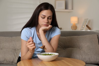 Eating disorder. Sad woman holding spoon with granola over bowl indoors