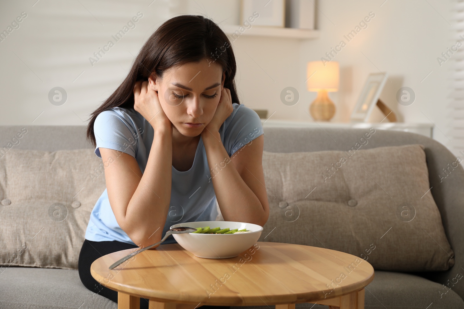 Photo of Eating disorder. Sad woman near bowl with meal at wooden table indoors