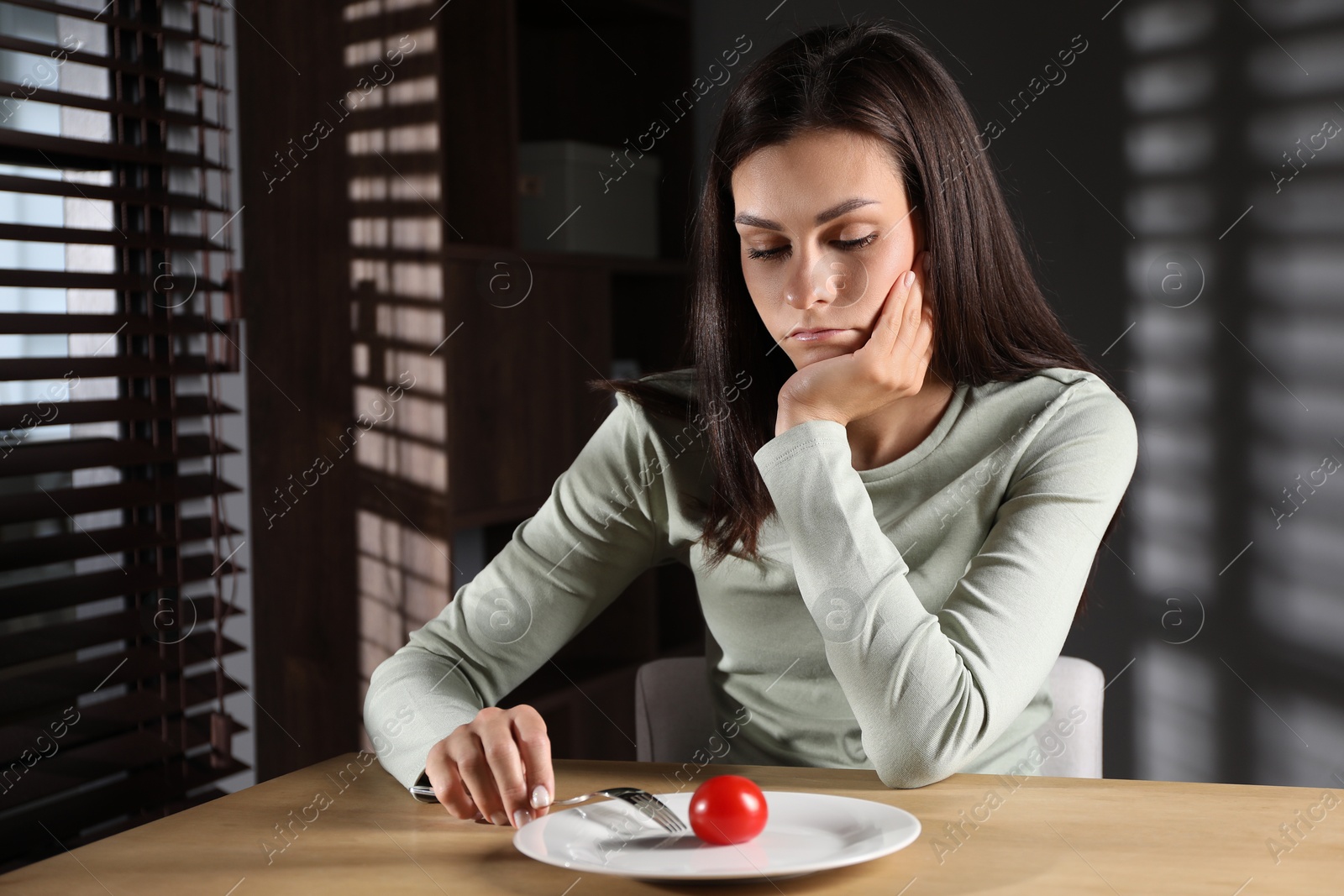 Photo of Eating disorder. Sad woman with fork near tomato at wooden table