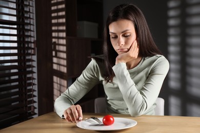 Eating disorder. Sad woman with fork near tomato at wooden table