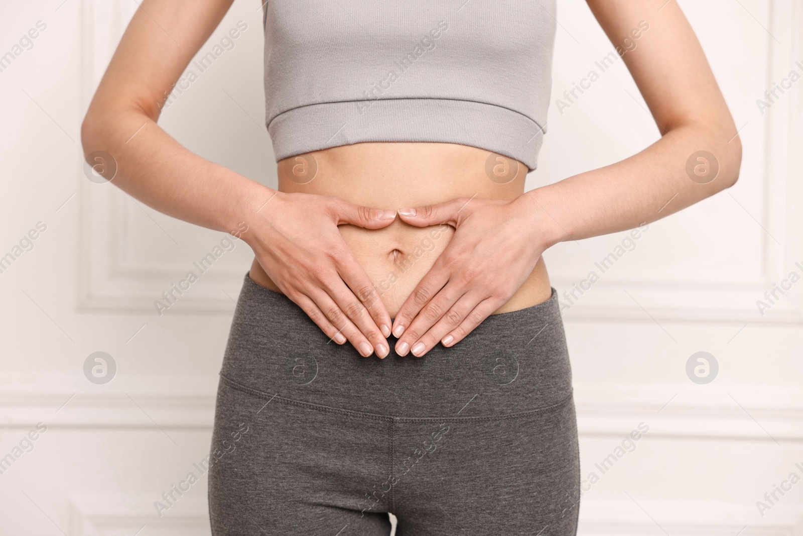 Photo of Healthy digestion. Woman making heart shape with hands near her belly indoors, closeup