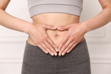 Healthy digestion. Woman making heart shape with hands near her belly indoors, closeup