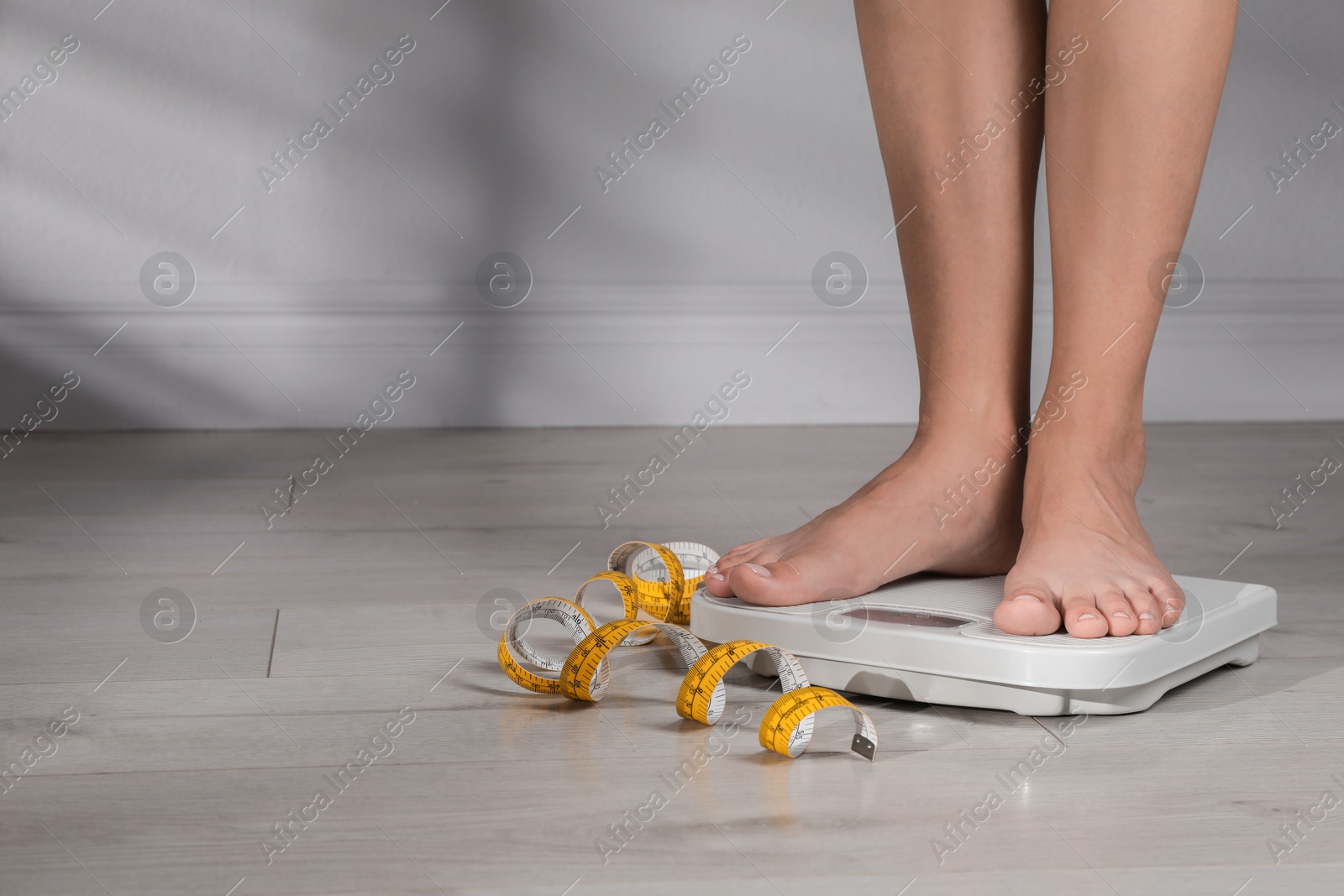 Photo of Eating disorder. Woman standing on floor scale and measuring tape indoors, closeup. Space for text