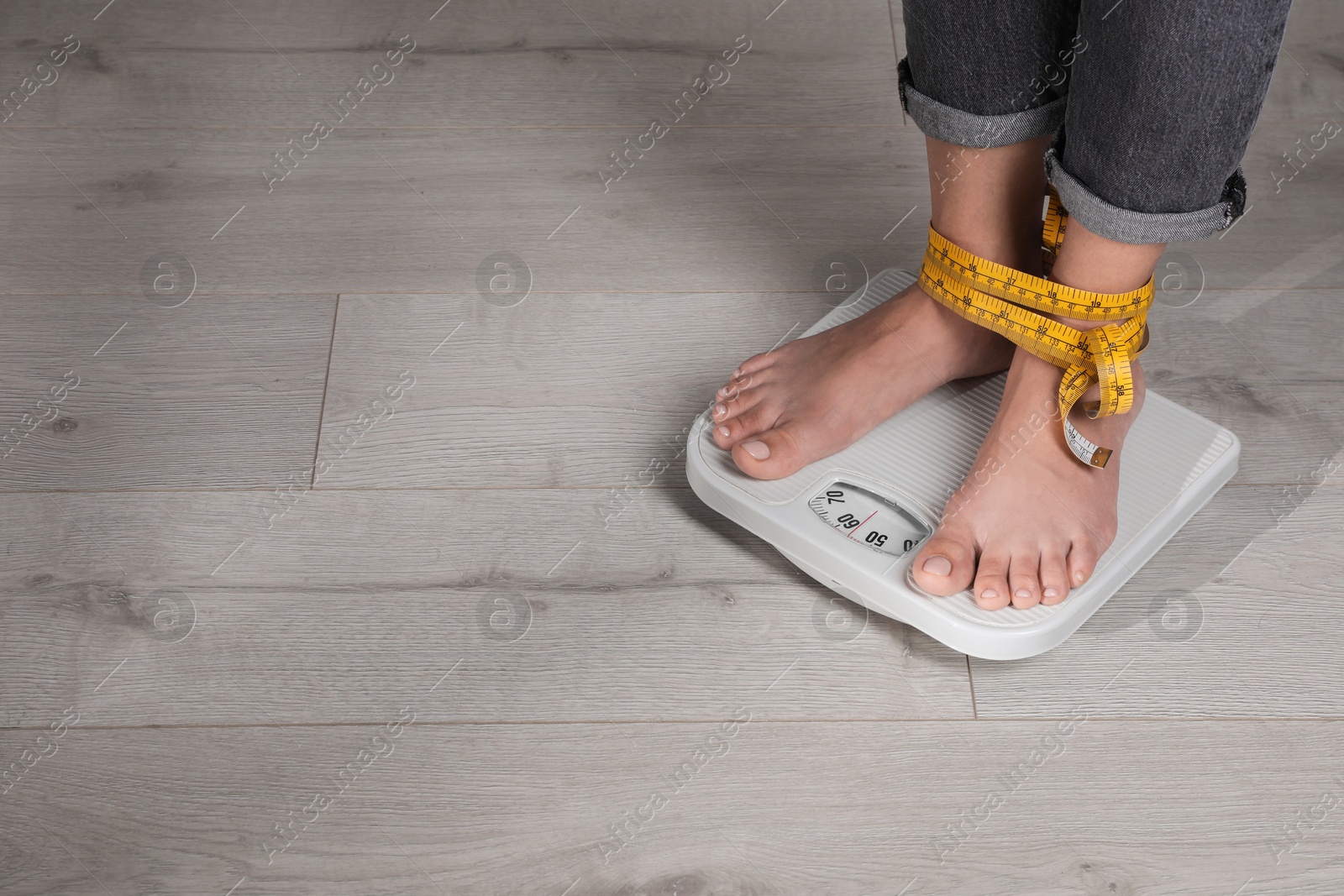 Photo of Eating disorder. Woman tied with measuring tape standing on floor scale indoors, closeup. Space for text