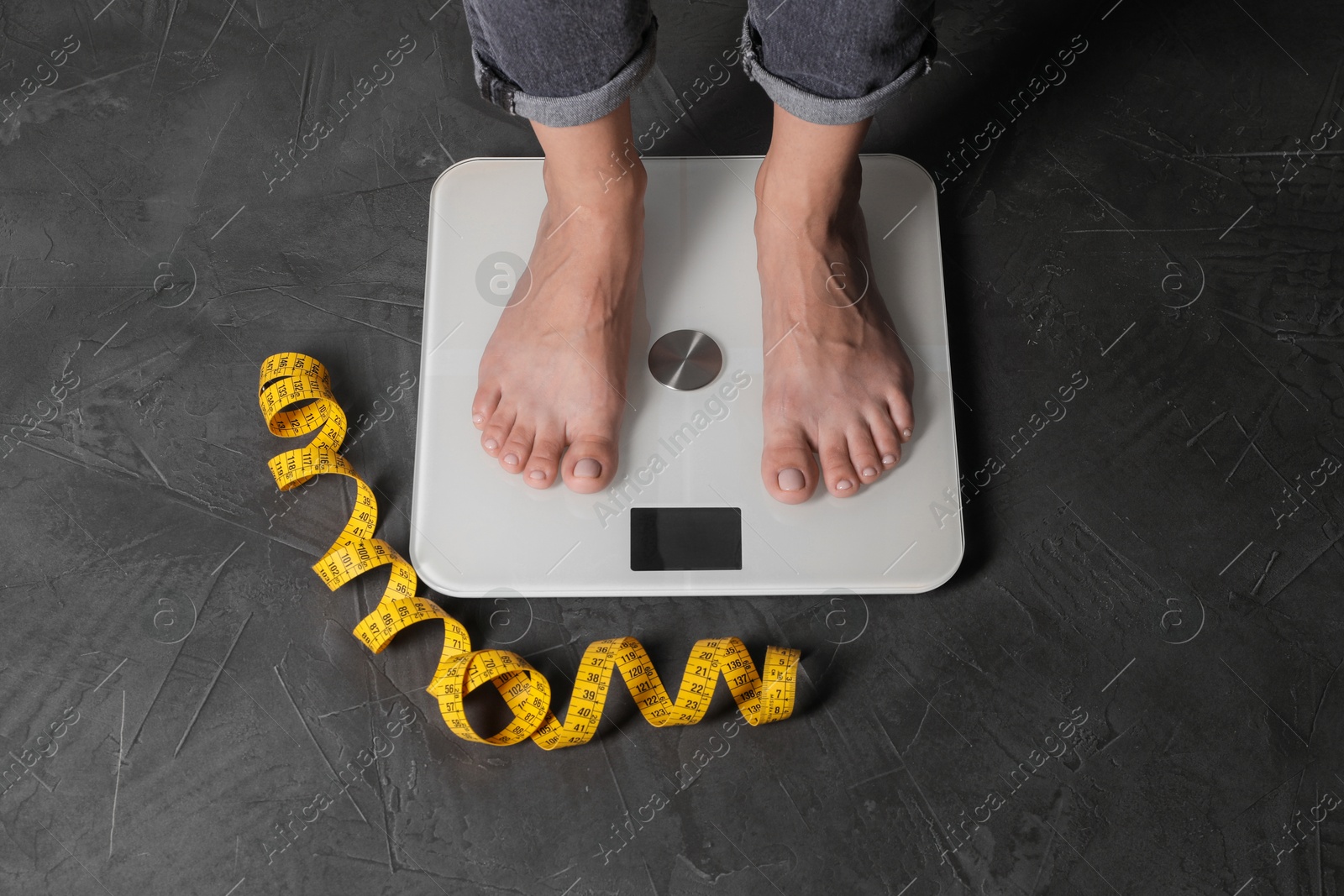 Photo of Eating disorder. Woman standing on floor scale and measuring tape indoors, above view