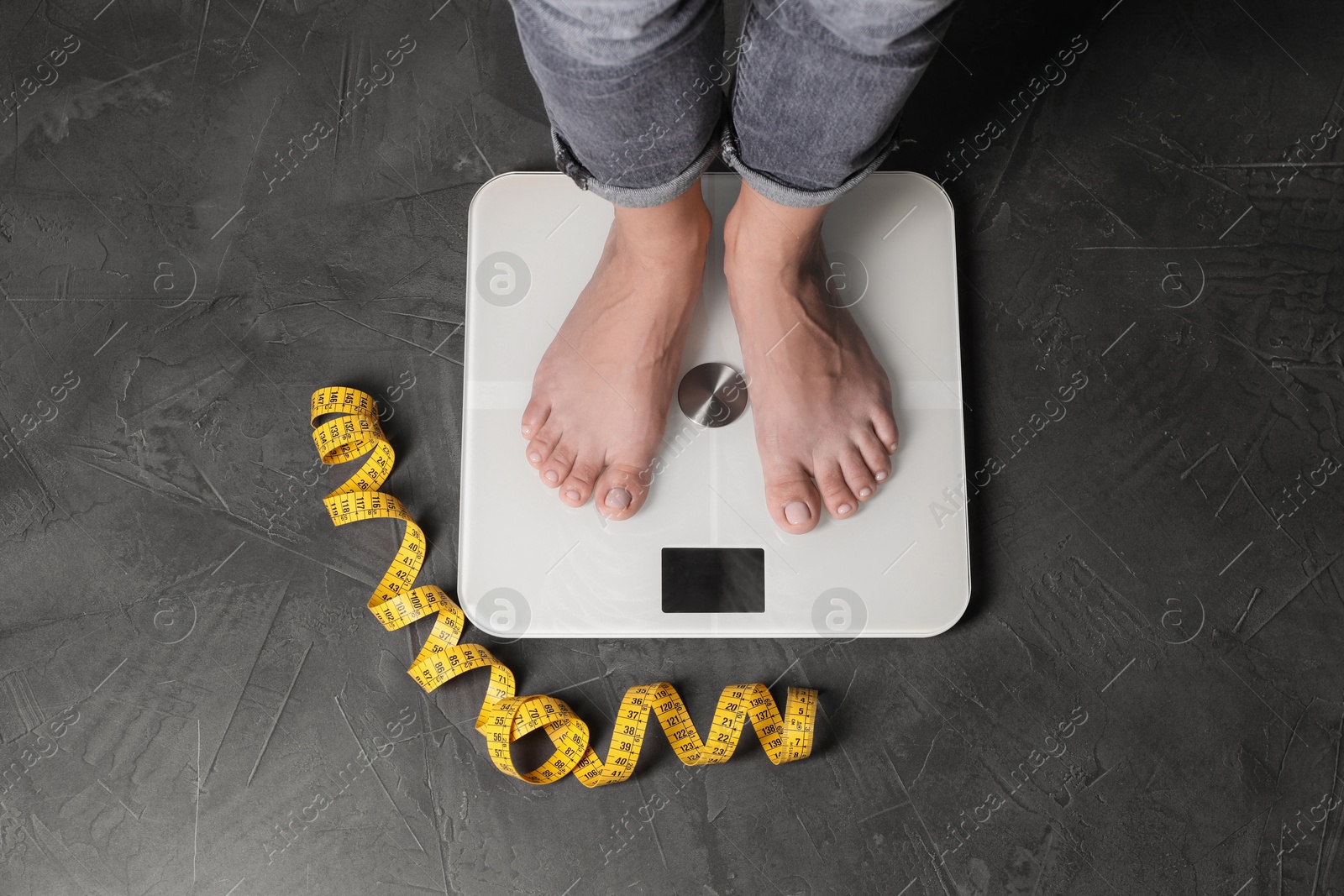 Photo of Eating disorder. Woman standing on floor scale and measuring tape indoors, top view