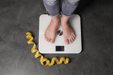 Eating disorder. Woman standing on floor scale and measuring tape indoors, top view