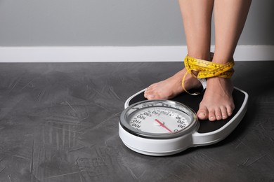 Photo of Eating disorder. Woman tied with measuring tape standing on floor scale indoors, closeup. Space for text