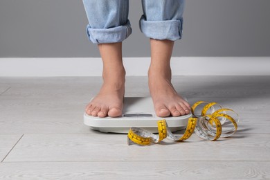 Eating disorder. Woman standing on floor scale and measuring tape indoors, closeup