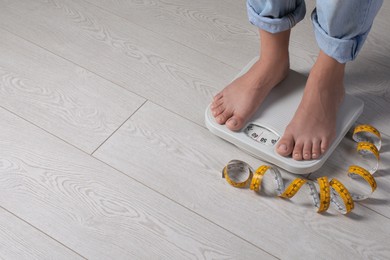 Eating disorder. Woman standing on floor scale and measuring tape indoors, closeup