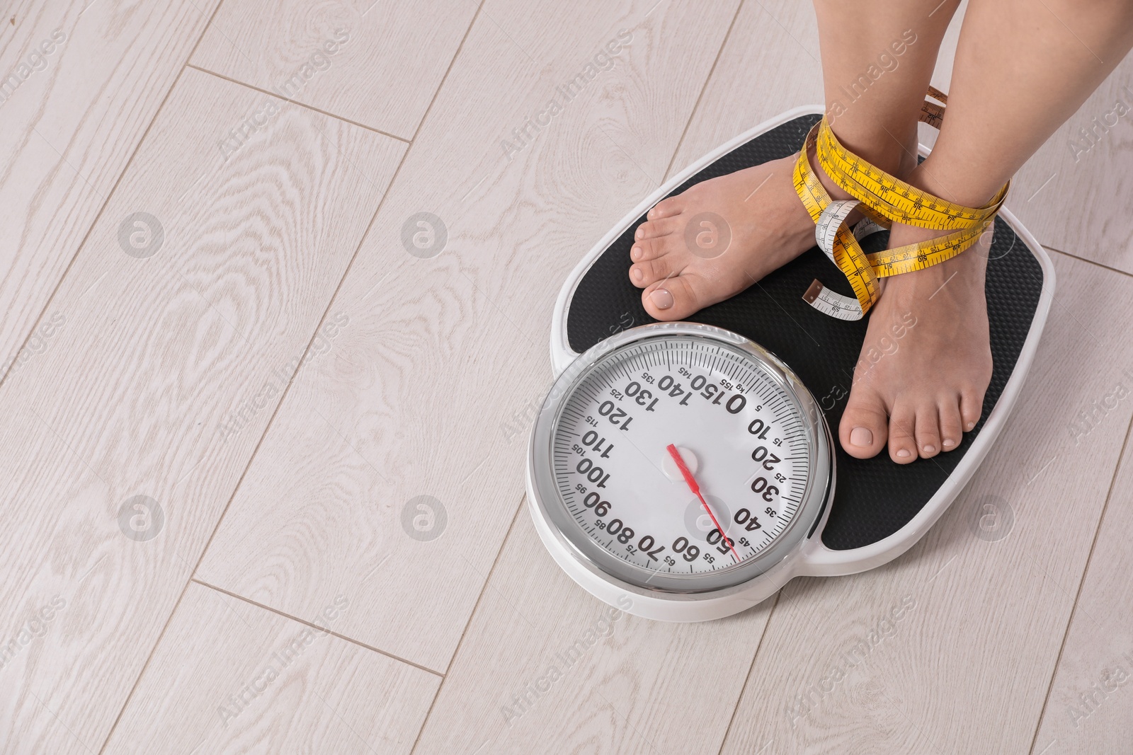 Photo of Eating disorder. Woman tied with measuring tape standing on floor scale indoors, closeup. Space for text