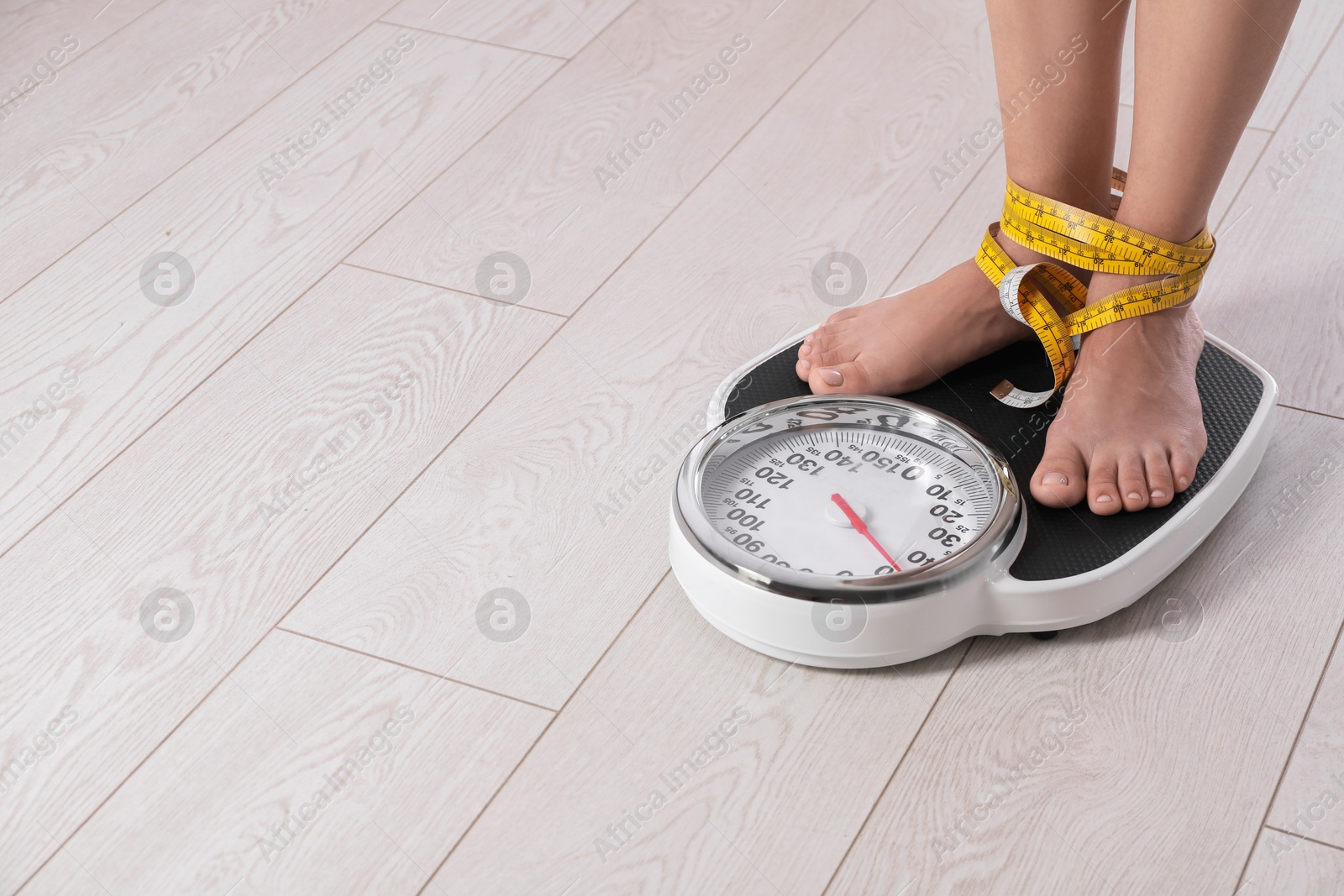 Photo of Eating disorder. Woman tied with measuring tape standing on floor scale indoors, closeup. Space for text