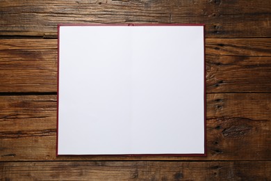 Photo of Open hardcover notebook with empty sheets on wooden table, top view. Mockup for design