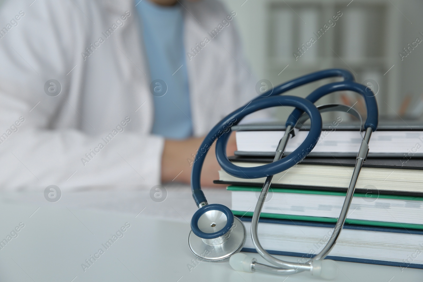 Photo of Doctor at white table in hospital, focus on medical stethoscope and books