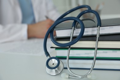 Photo of Doctor at white table in hospital, focus on medical stethoscope and books