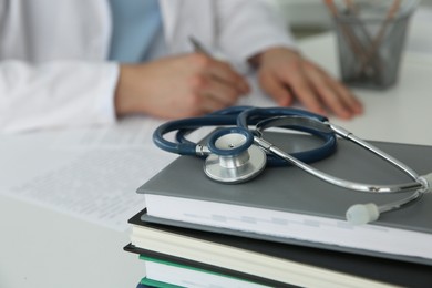 Photo of Doctor at white table in hospital, focus on medical stethoscope and books