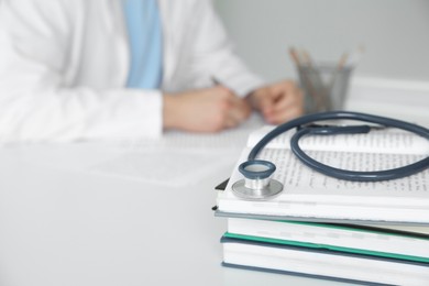 Photo of Doctor at white table in hospital, focus on medical stethoscope and books