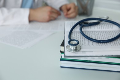 Photo of Doctor at white table in hospital, focus on medical stethoscope and books