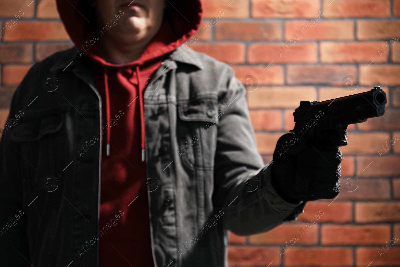 Photo of Dangerous criminal with gun near brick wall, closeup. Armed robbery