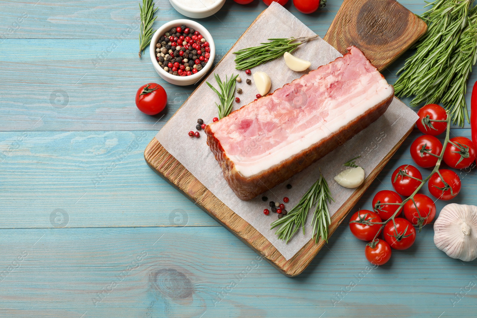 Photo of Piece of raw bacon with spices and tomatoes on light blue wooden table, flat lay. Space for text