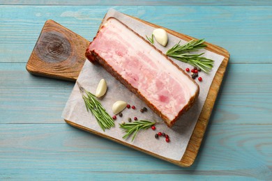 Photo of Piece of raw bacon with spices and rosemary on light blue wooden table, top view