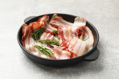 Photo of Delicious bacon slices and fresh rosemary in frying pan on light grey table