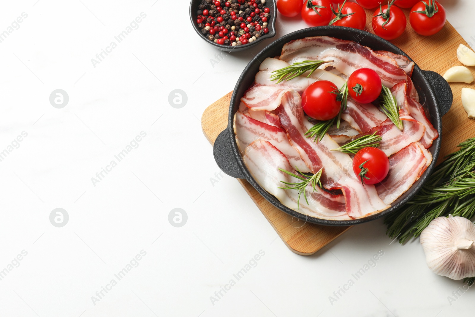 Photo of Delicious bacon slices in frying pan, spices and tomatoes on white table, flat lay. Space for text