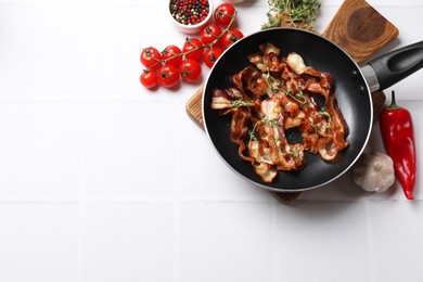 Photo of Delicious bacon slices in frying pan and products on white tiled table, flat lay. Space for text