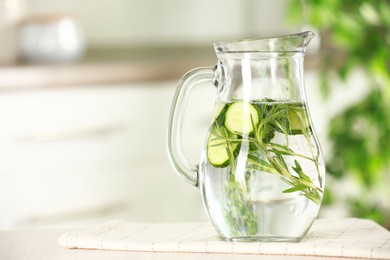 Refreshing cucumber water with rosemary in jug on white table, closeup. Space for text