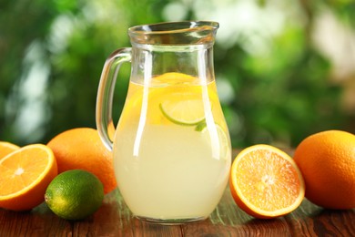 Photo of Refreshing lemonade with citruses in jug among fruits on wooden table against blurred green background