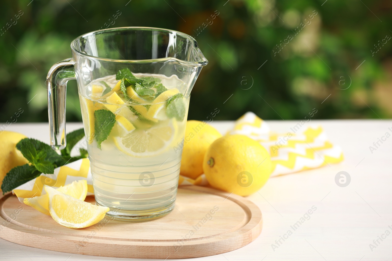 Photo of Refreshing lemonade with mint in jug on light table against blurred green background. Space for text