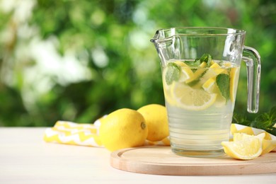 Photo of Refreshing lemonade with mint in jug on light table against blurred green background. Space for text