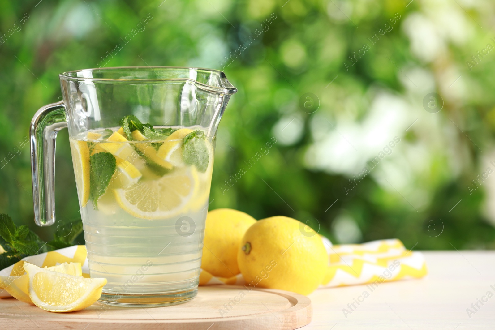 Photo of Refreshing lemonade with mint in jug on light table against blurred green background. Space for text