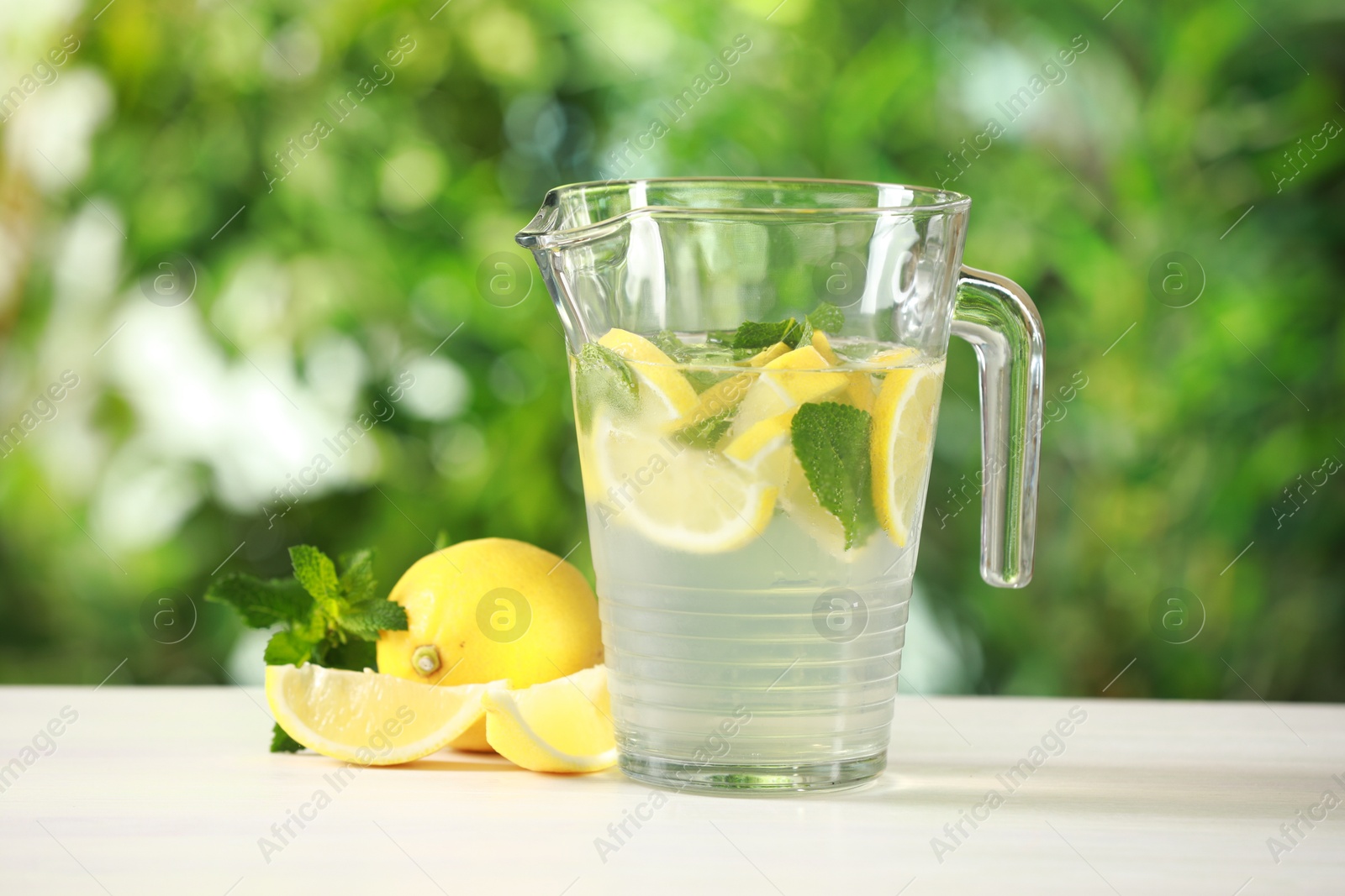 Photo of Refreshing lemonade with mint in jug on light table against blurred green background