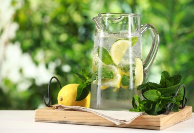 Photo of Refreshing lemonade with mint in jug and citrus fruit on light table against blurred green background, closeup