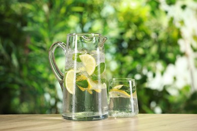 Refreshing lemonade with mint in jug and glass on wooden table against blurred green background