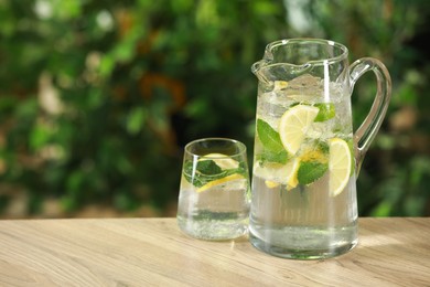 Photo of Refreshing lemonade with mint in jug and glass on wooden table against blurred green background. Space for text