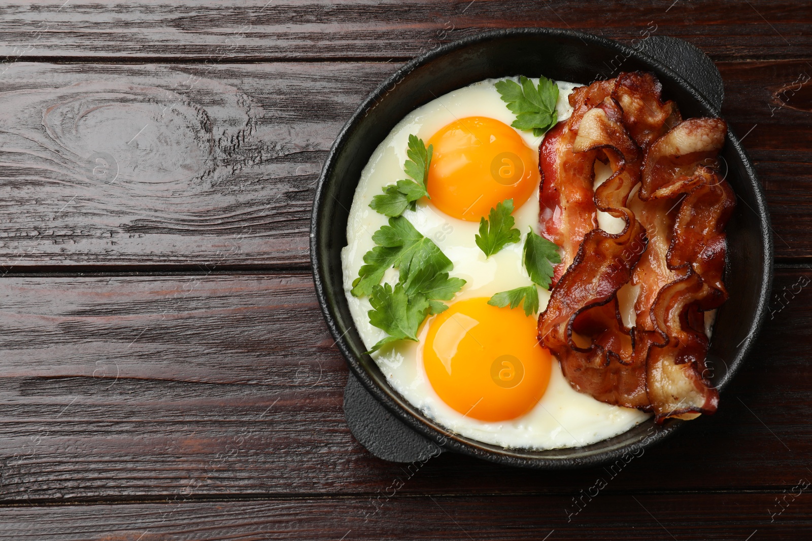 Photo of Tasty bacon, eggs and parsley on wooden table, top view. Space for text