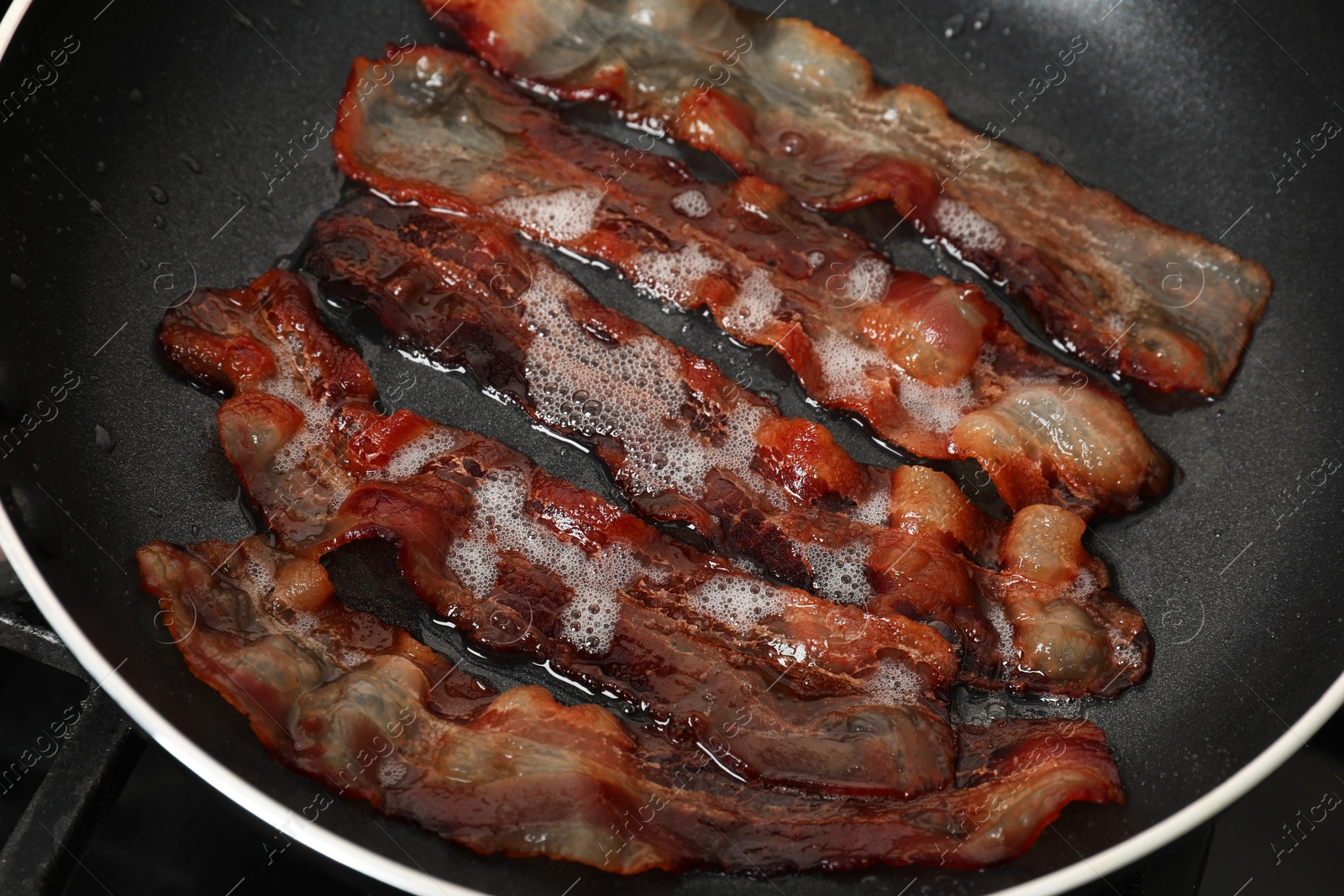 Photo of Slices of bacon frying in pan, closeup